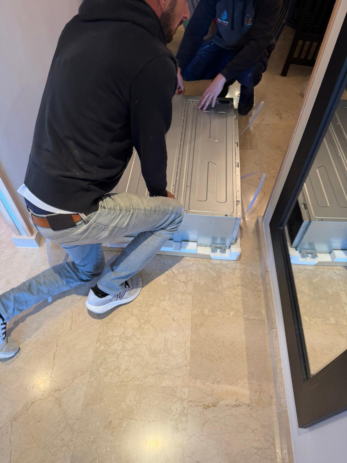 Two Agua Therm technicians lifting the new Johnson indoor unit into the false ceiling