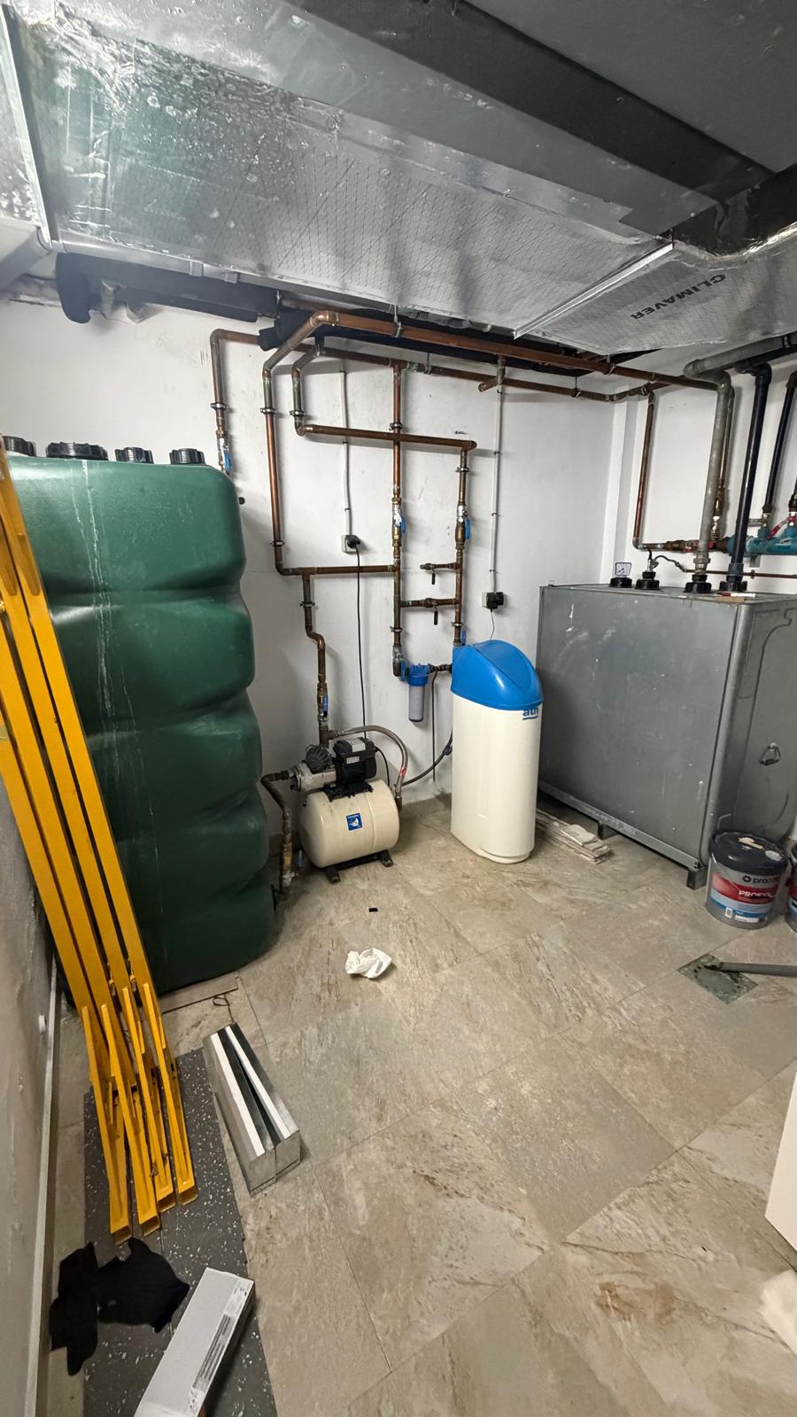 Plant room overview before installation — large green oil storage tank, water softener, pressure pump and copper pipework in La Cala de Mijas villa before Agua Therm heat pump conversion