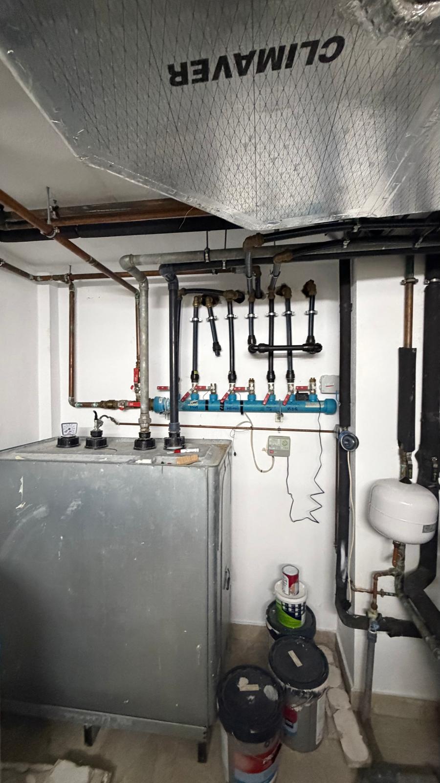 Grey oil boiler unit with blue hydraulic manifold, expansion vessel and copper pipework — existing heating system before decommissioning in La Cala de Mijas villa