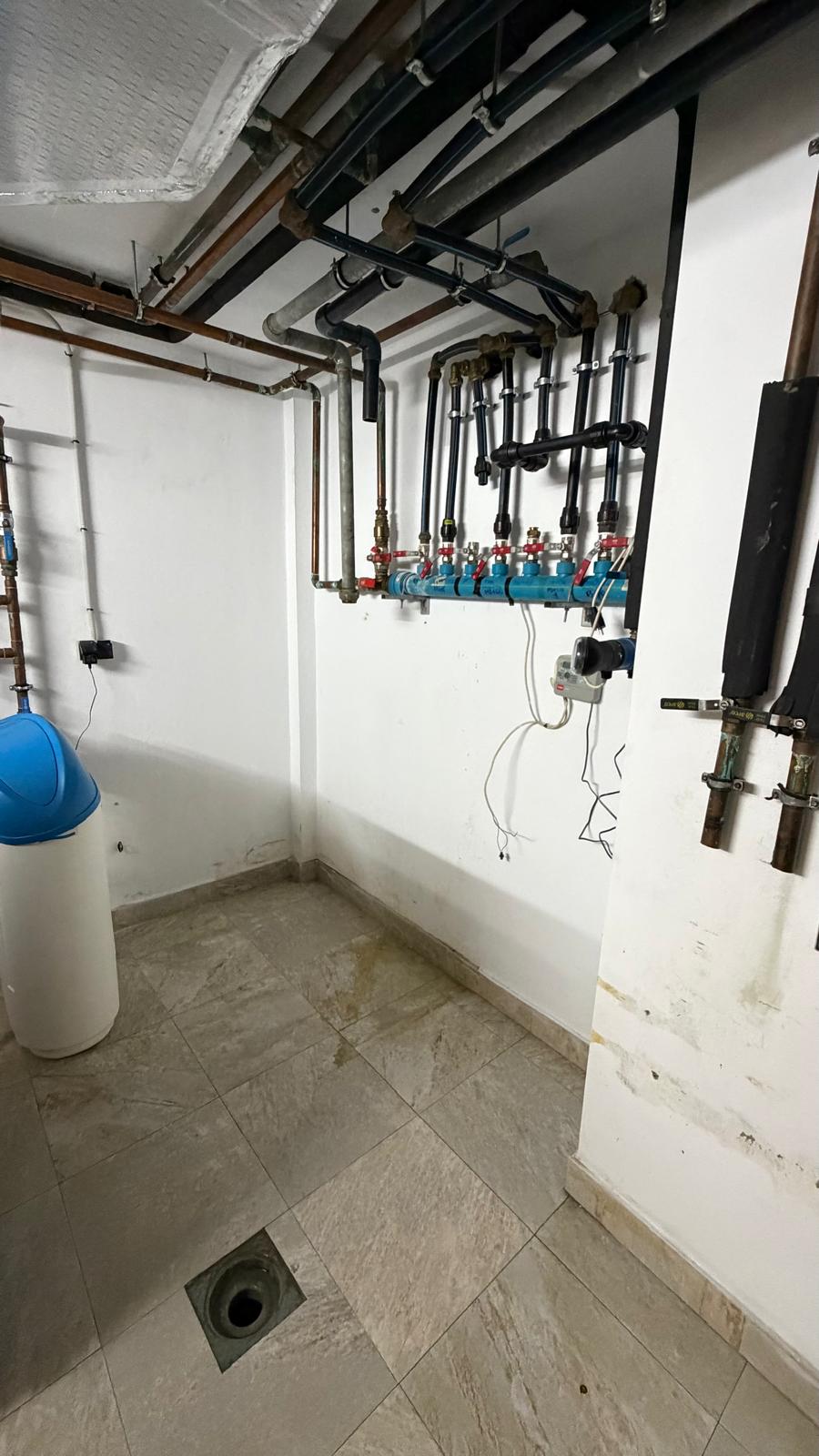 La Cala de Mijas plant room after oil boiler removal — cleared room with new black pipework distribution system and retained water softener, no oil tank, clean professional installation by Agua Therm