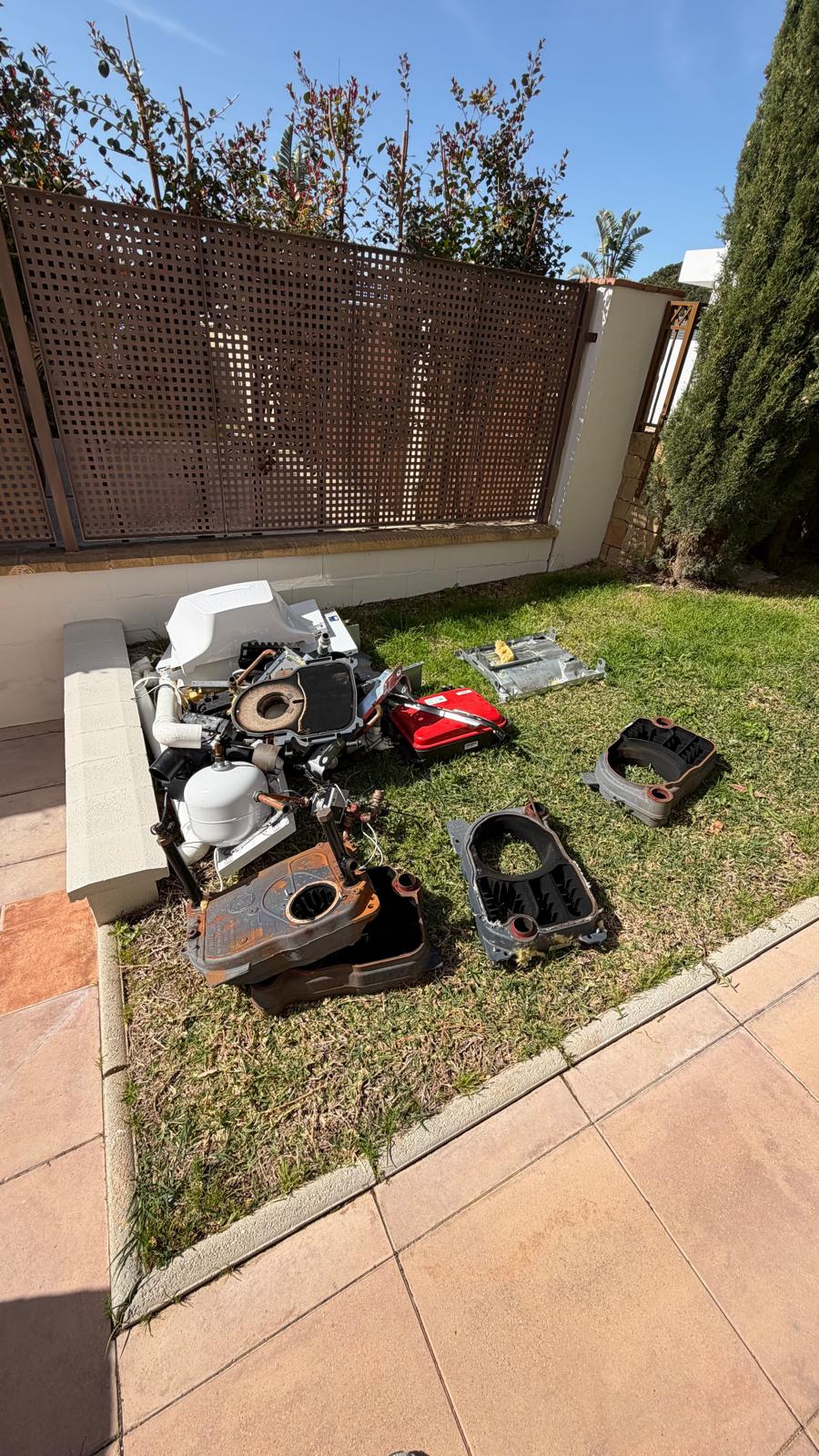Decommissioned Baxi oil boiler components removed from La Cala de Mijas villa — burner assembly, expansion vessel, manifold headers and boiler casings laid out in garden before authorised collection and disposal by licensed waste contractor
