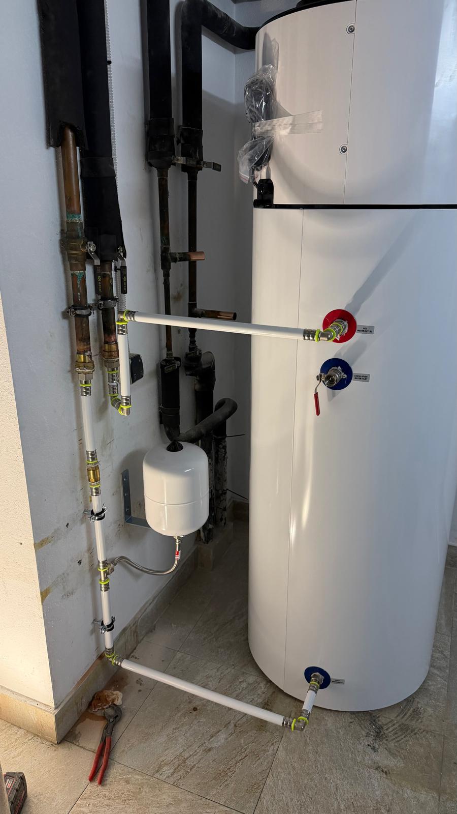 Daitsu heat pump connections showing hot water inlet and outlet ports (red and blue), domestic hot water expansion vessel, and new white connection pipework — professional Agua Therm installation La Cala de Mijas