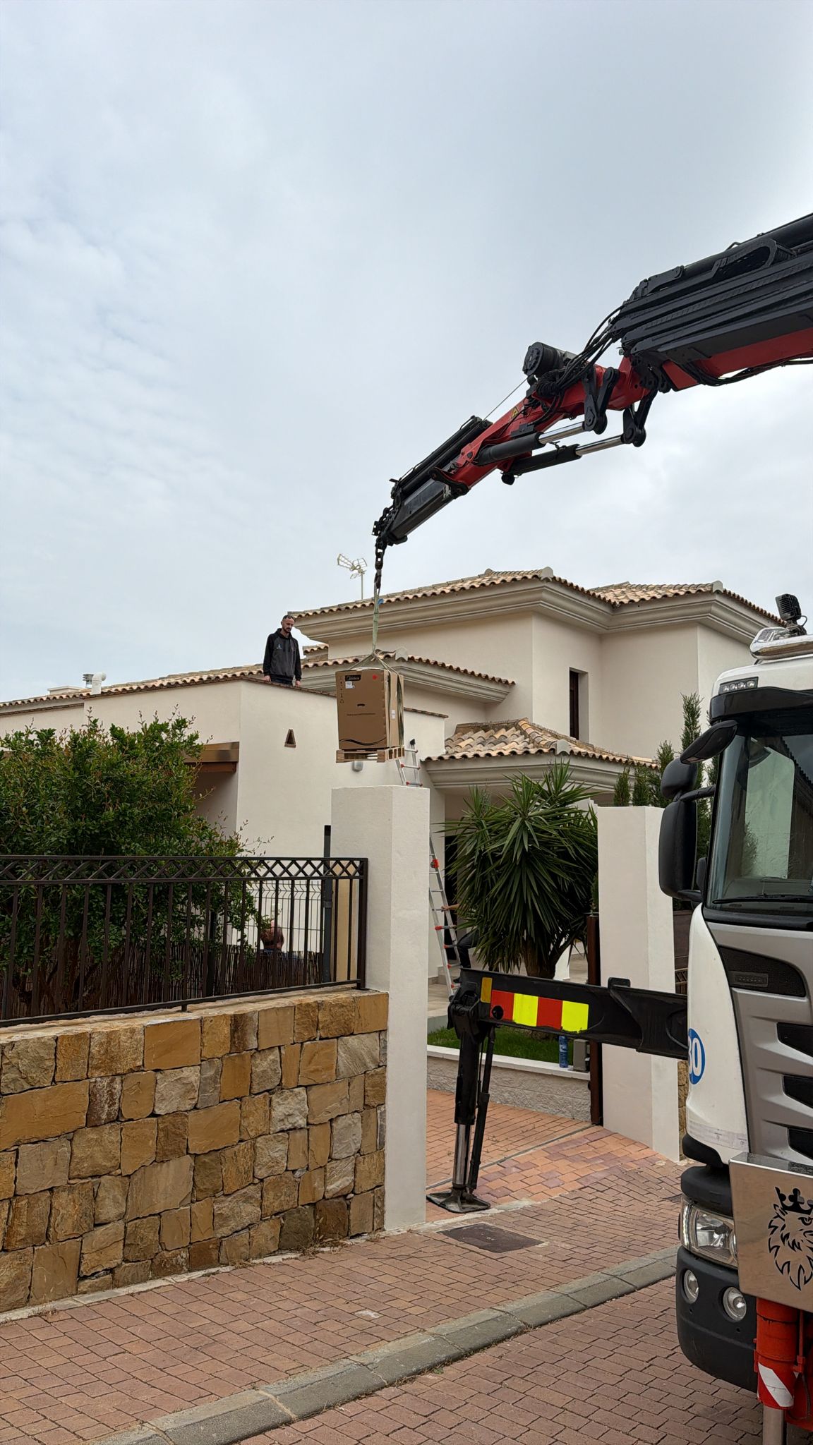 Palfinger crane hoisting new heat pump outdoor unit to rooftop of La Cala de Mijas villa — Agua Therm technician guiding unit on rooftop during crane delivery, professional HVAC installation Costa del Sol
