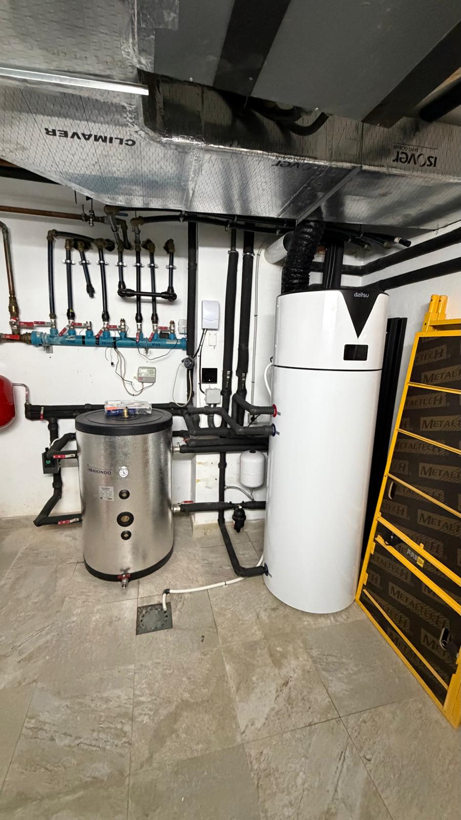 Complete view of La Cala de Mijas plant room after installation — Ibaiondo buffer left, Daitsu aerothermal right, blue hydraulic manifold, black insulated pipework, Climaver ductwork on ceiling