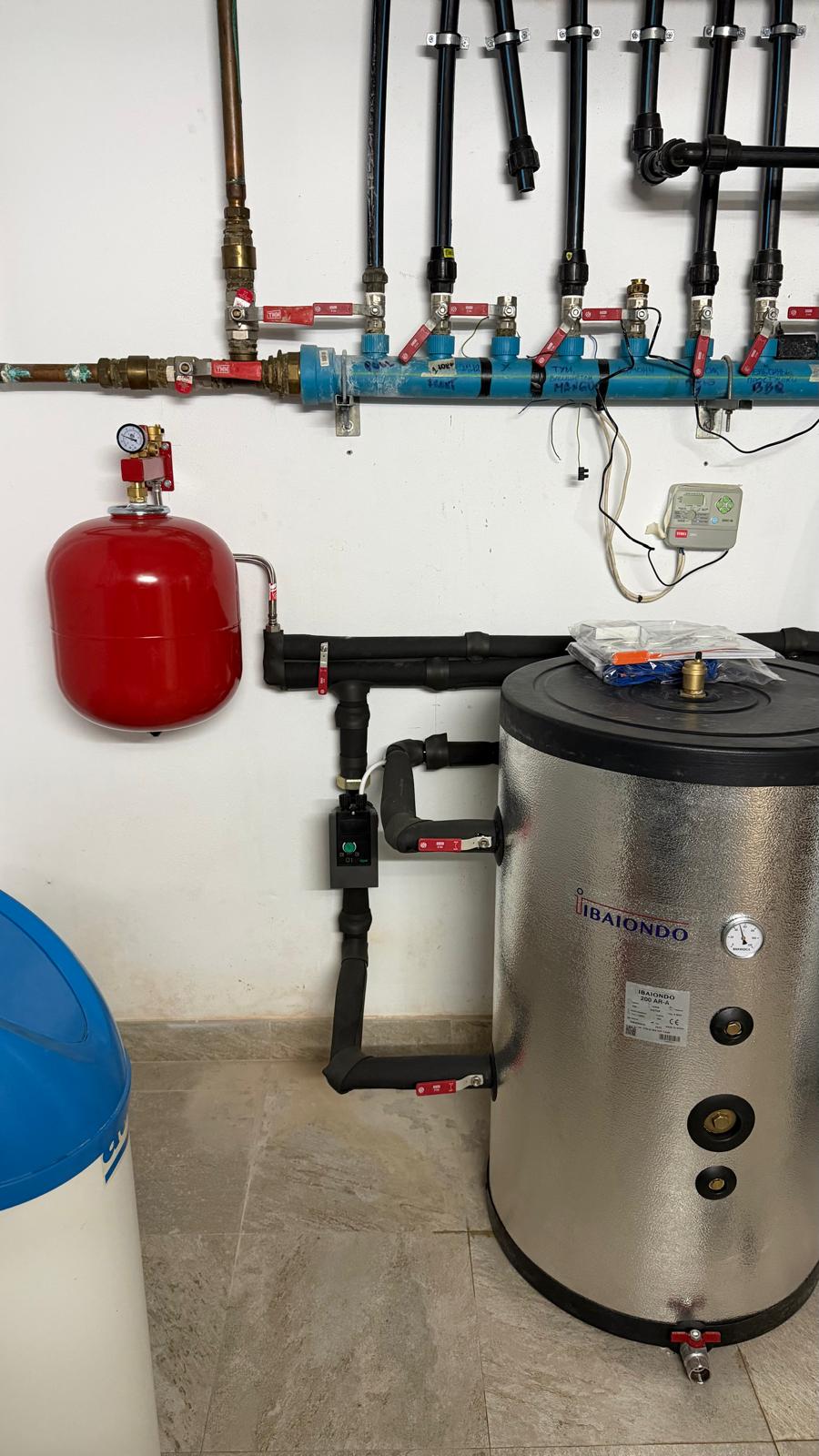 Ibaiondo buffer tank with blue hydraulic manifold, red expansion vessel, blue and white water softener — La Cala de Mijas plant room fully equipped after Agua Therm heat pump installation