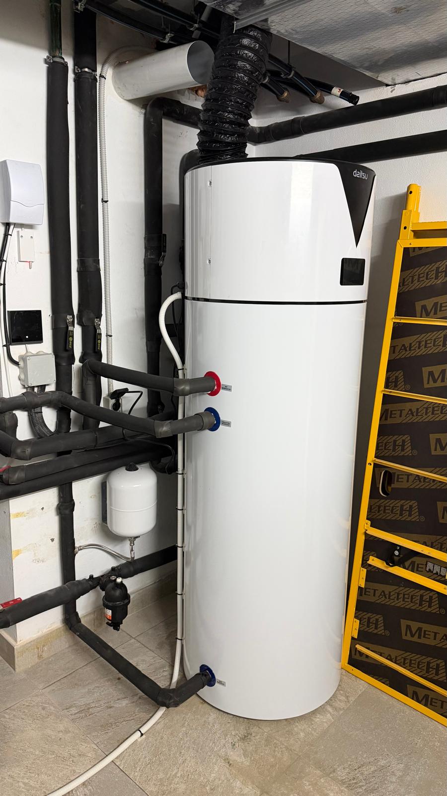 Side view of Daitsu aerothermal unit in La Cala de Mijas plant room — red and blue DHW connections visible, small expansion vessel, new black insulated pipework to left
