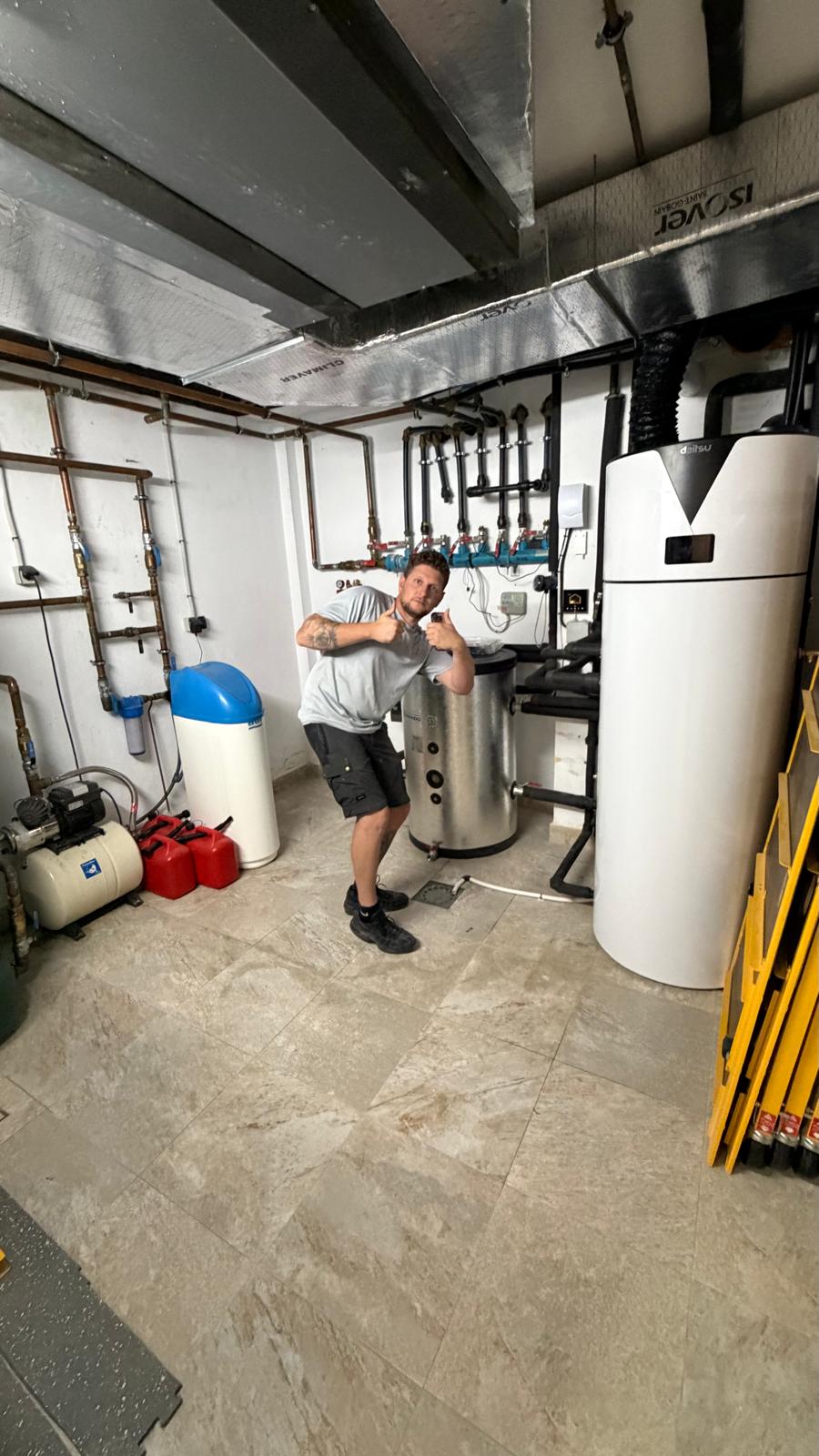 Agua Therm technician giving thumbs up in front of completed heat pump system in La Cala de Mijas — Ibaiondo buffer, Daitsu aerothermal, water softener and distribution manifold visible — job complete