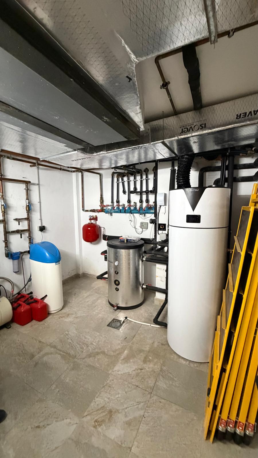 La Cala de Mijas plant room fully complete — blue/white water softener left, Ibaiondo buffer centre-left, red expansion vessel, Daitsu aerothermal unit right, blue manifold on wall, silver ductwork on ceiling — complete heat pump system installed by Agua Therm