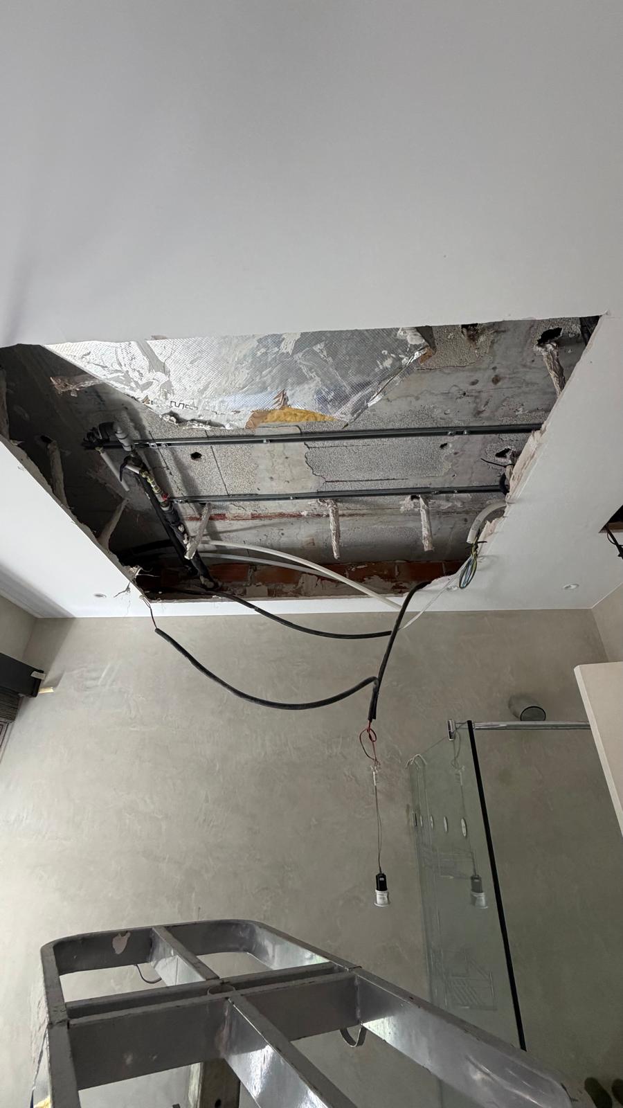 Segundo baño con plenum abierto sobre la zona de ducha — forjado de hormigón y conductos heredados expuestos