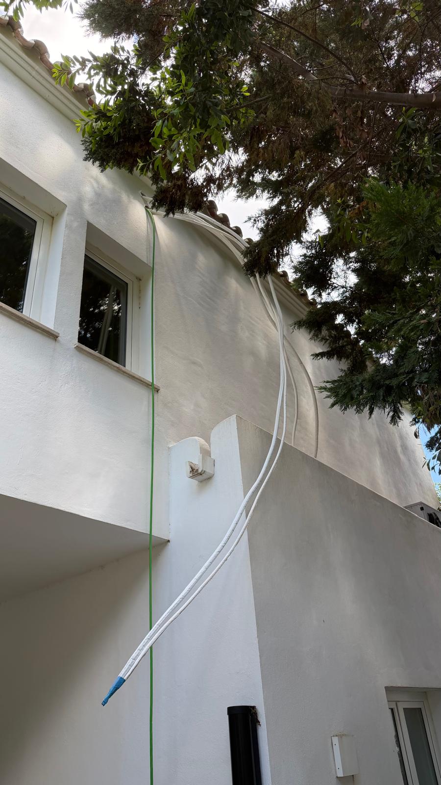 Línea frigorífica aislada subiendo dos plantas por pared blanca enfoscada hasta bajo las tejas árabes