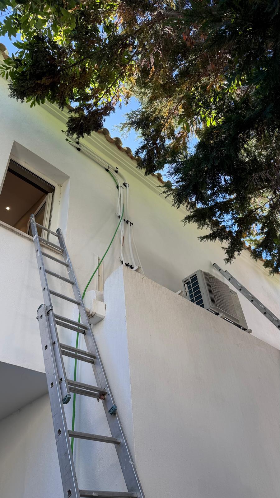 Unidad exterior Daikin en planta alta con escalera de aluminio y línea frigorífica grapada bajo el alero