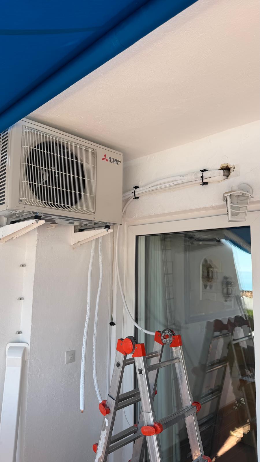 New Mitsubishi Electric outdoor unit being wall-mounted on balcony during installation in Torremolinos