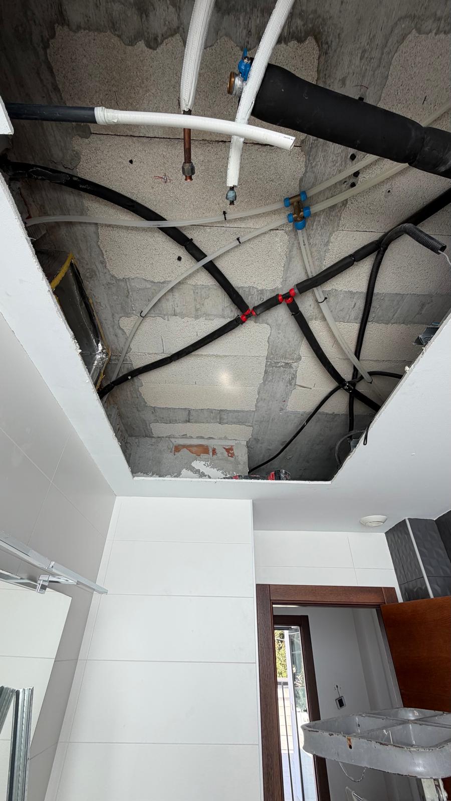 Ceiling void opened showing existing villa concrete block construction, insulated refrigerant lines (black), white plumbing pipes and Airzone actuator wiring