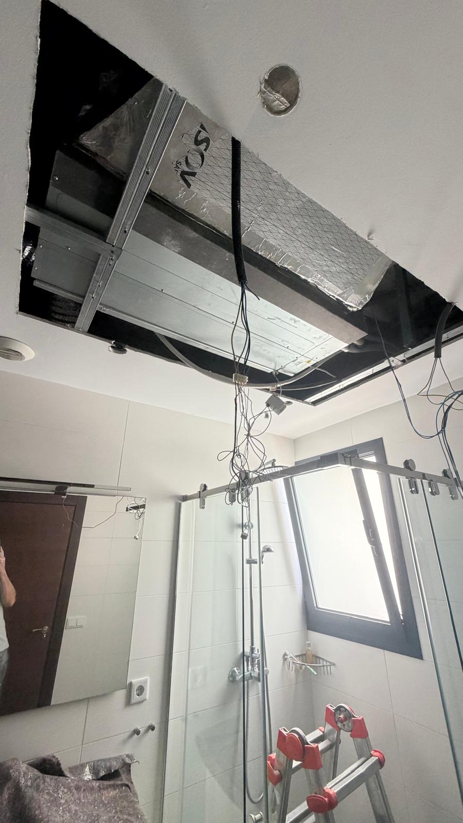 Daikin ADEA50A2VEB indoor unit installed in bathroom ceiling void, ADSI foil duct insulation visible, Airzone control wiring hanging down, glass shower screen below
