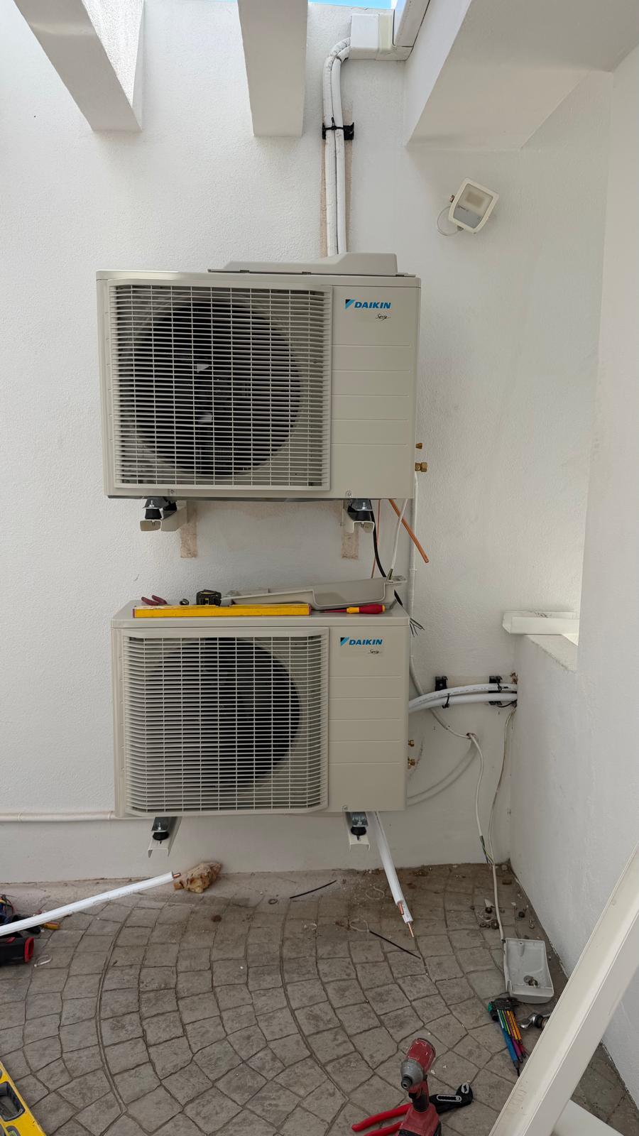 Both Daikin ARXM35A5V1B9 outdoor units wall-mounted stacked on villa side elevation, line set routing upward, installation in progress with tools on ground