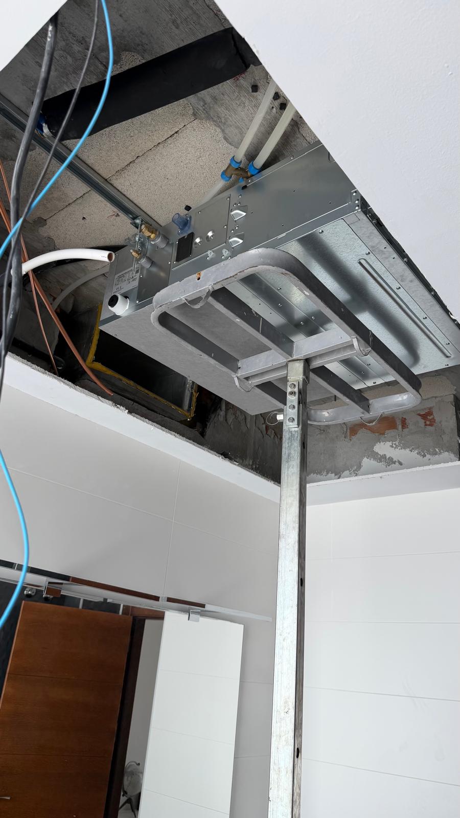 Daikin indoor unit being raised into ceiling void supported by steel acrow prop, blue and orange refrigerant lines visible in background