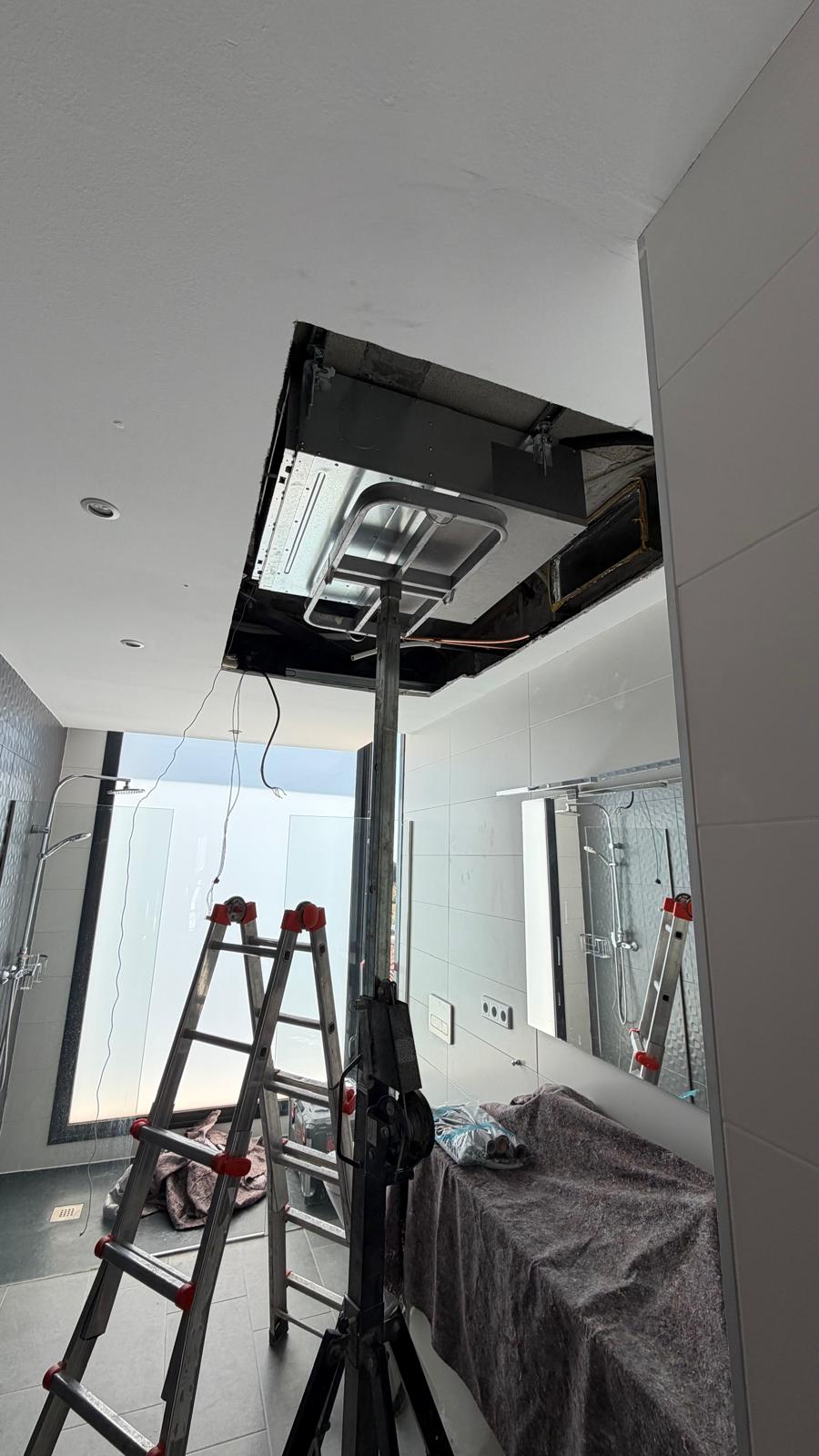 Master bathroom en-suite: indoor unit in ceiling access opening, two ladders and protective work table in place, large glass shower screen visible