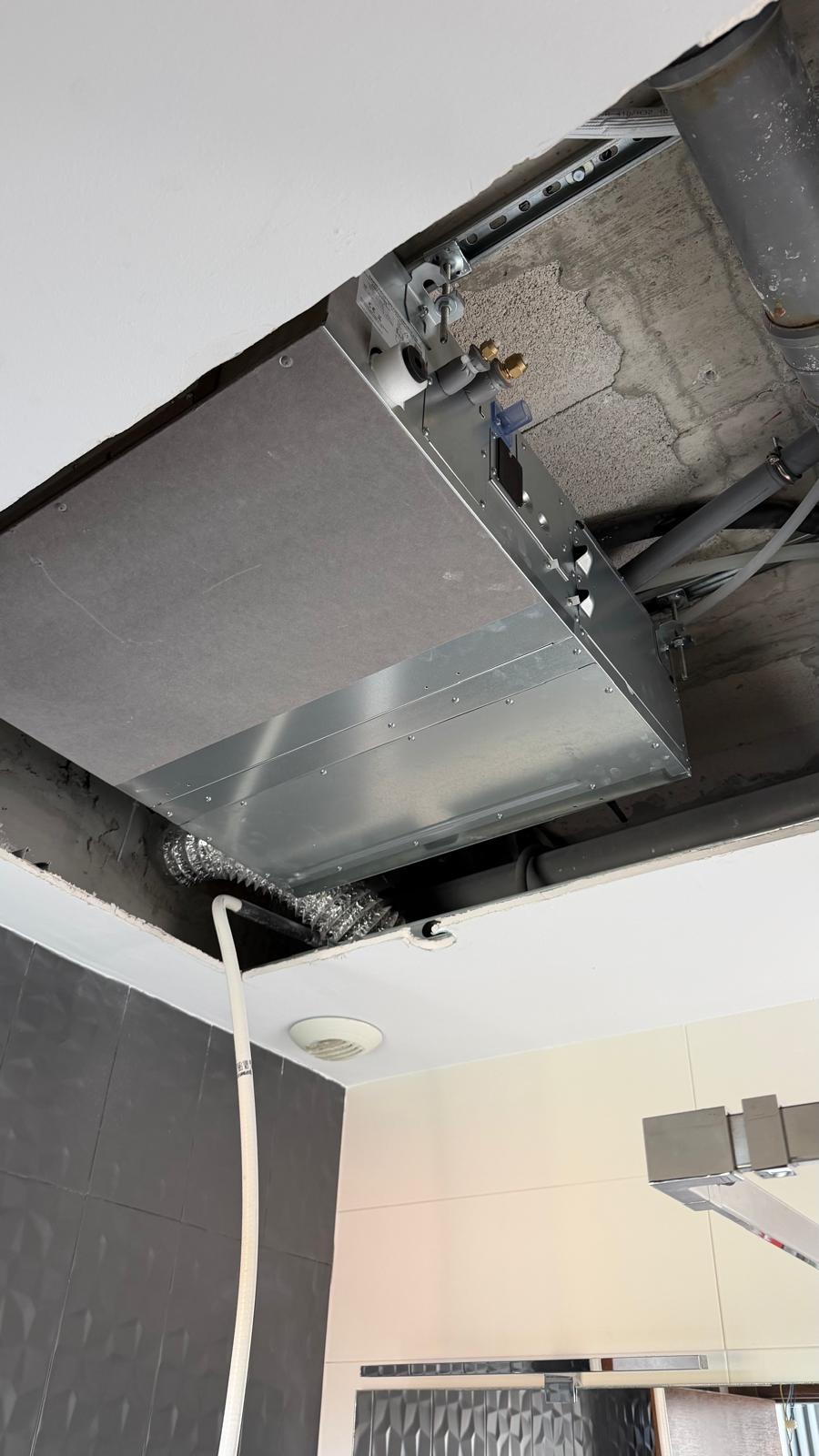 Daikin unit installed in third room: aluminium flex duct connection visible bottom-left, dark grey tile bathroom surround, supply grille aperture position