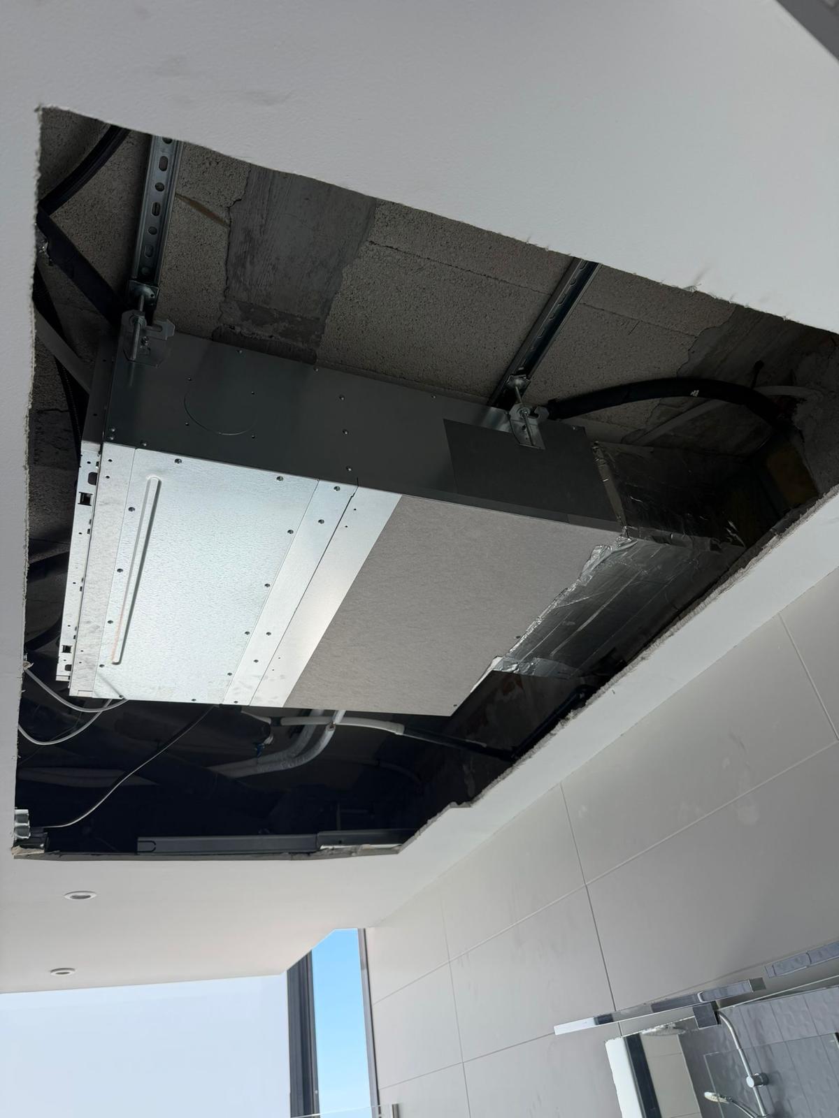 Indoor unit in ceiling void: unistrut ceiling channels, Airzone insulated ductwork plenum with aluminium tape (right), unit body, white tile bathroom and glass shower below