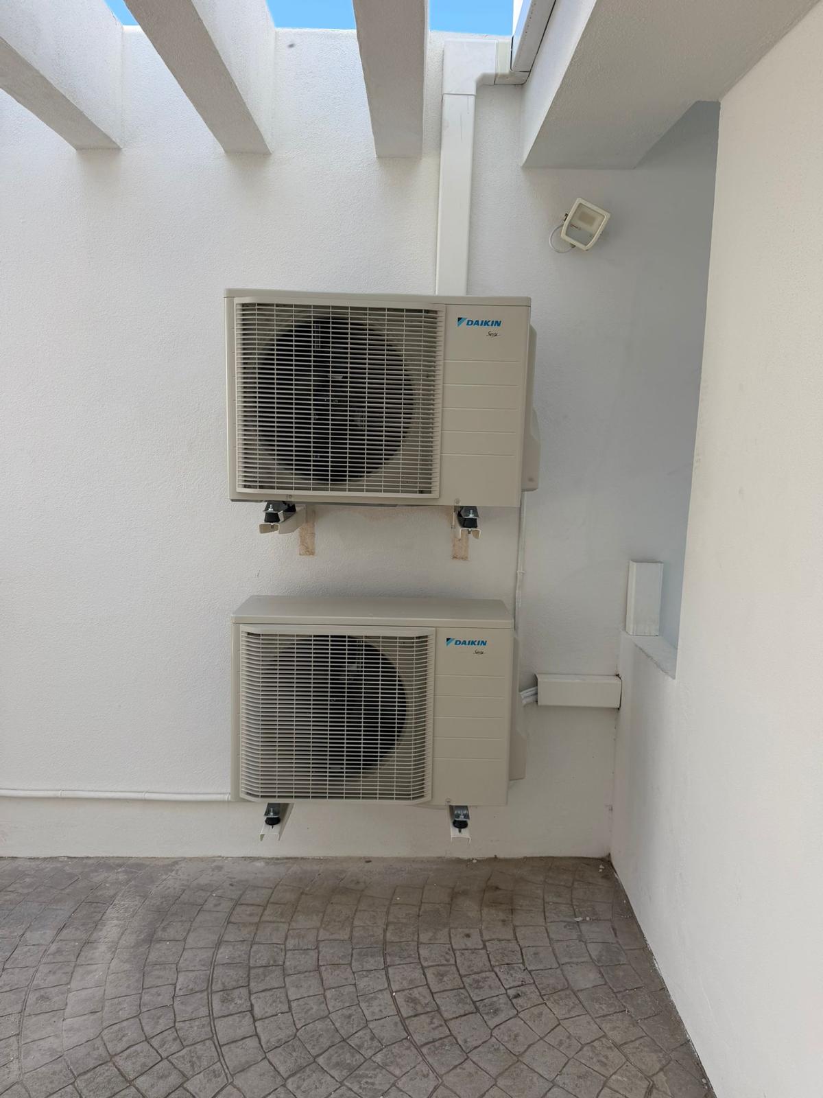 Completed installation: both Daikin ARXM35A5V1B9 outdoor units wall-mounted on villa side elevation, line sets in white trunking, cobblestone patio floor