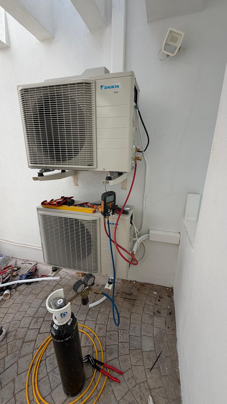 Commissioning: both outdoor units with Testo digital manifold gauge connected to service ports, nitrogen cylinder on floor with yellow hose, red and blue manifold hoses