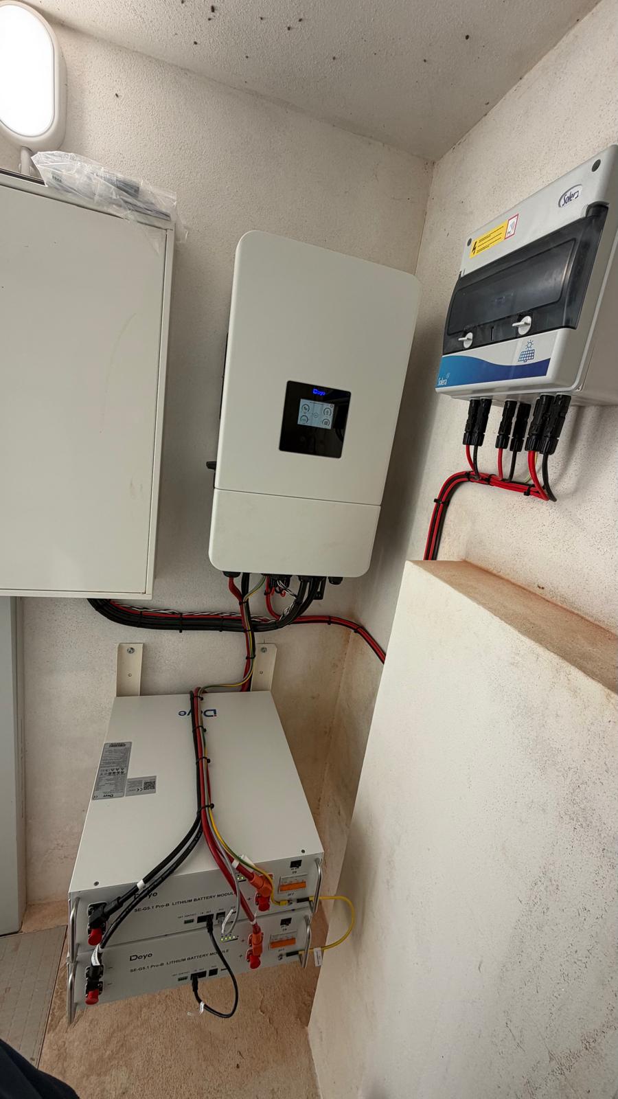 El inversor híbrido Deye conectado a dos módulos de batería Deye apilados, con aislamiento DC y cableado DC rojo/negro pulcramente peinado.