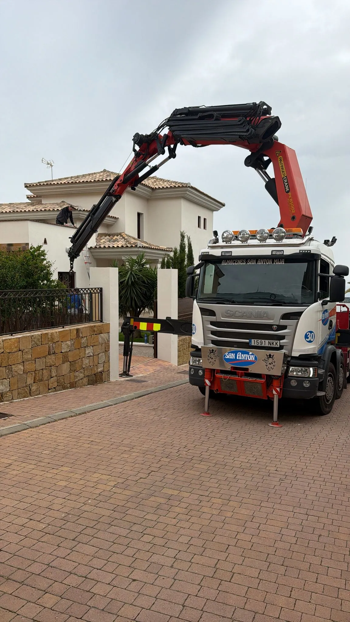 Camión grúa Scania rojo elevando equipos sobre una villa en Marbella