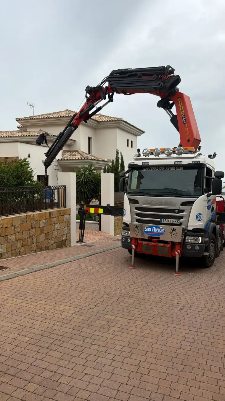 Red Scania crane truck lifting equipment over a luxury Marbella villa