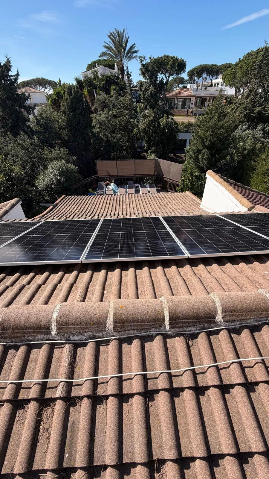 Solar panels on a terracotta tile roof with palm trees in Marbella